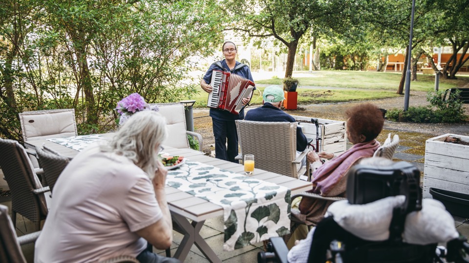 En person spelar dragspel för några personer på en uteplats.