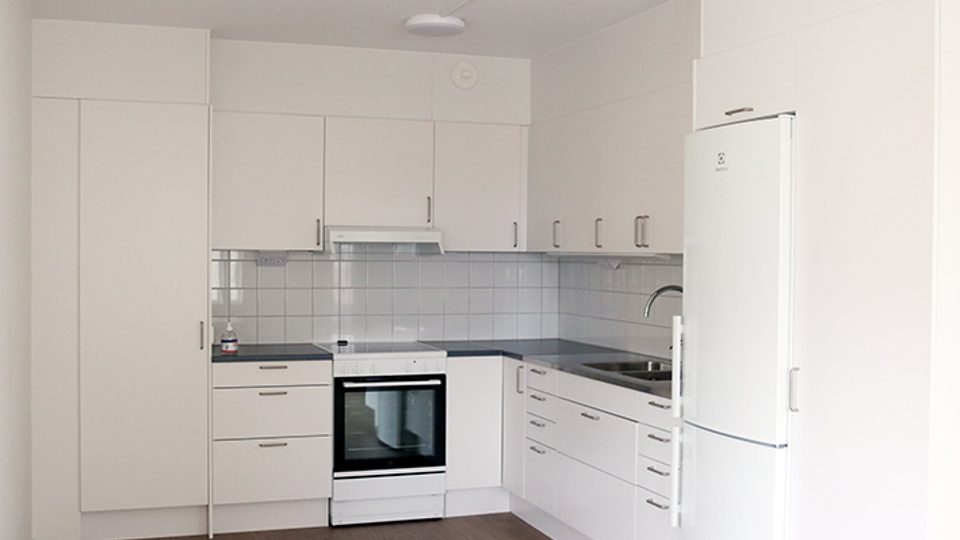 Ett vitt tomt kök med vita skåpluckor och en spishäll