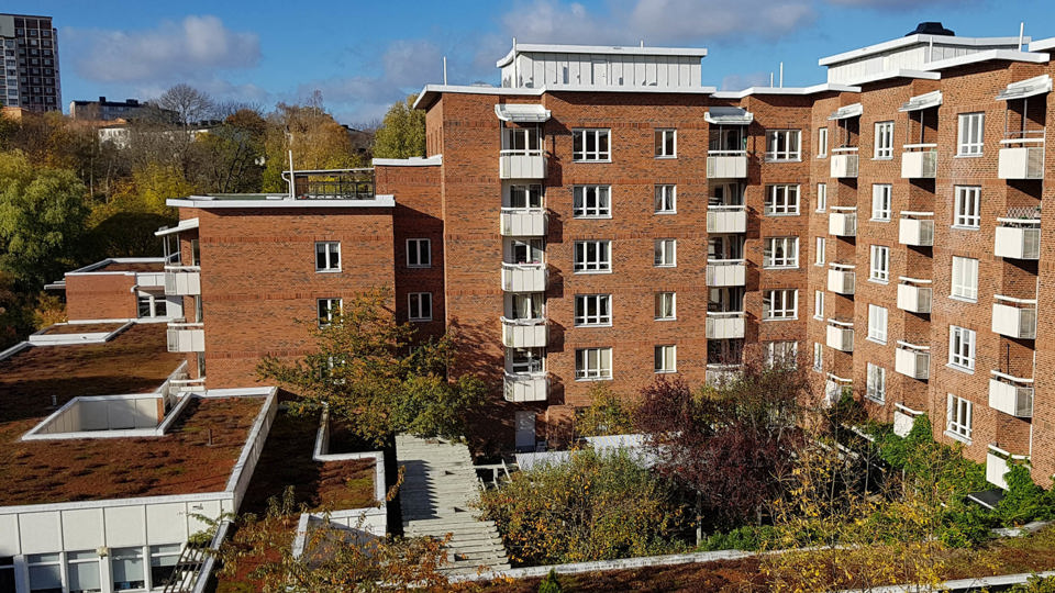 Högt tegelhus med vita balkonger och lummig uteplats.