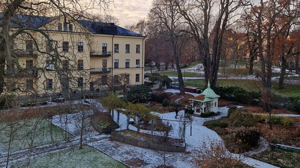 Gult stort hus intill en trädgård som heter Sinnenas trädgård. Det ligger snö på marken. Bakom trädgården skymtar en kulle i Vasaparken. 