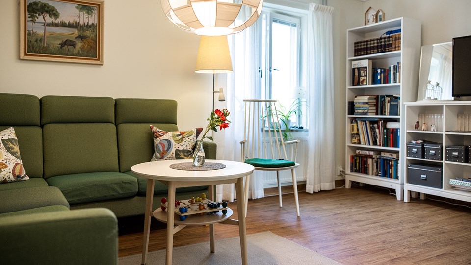 En hörnsoffa, soffbord, stol och bokhylla med böcker i ett rum med fönster.