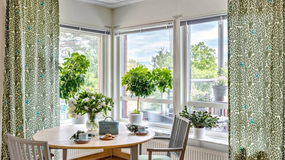 Ett dukat bord på gaveln med stora fönster, dukat för kaffe och kaka.