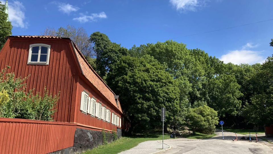 En väg som slutar i en vändplan vid ett gammalt rött hus med många fönster och gröna lummiga träd.