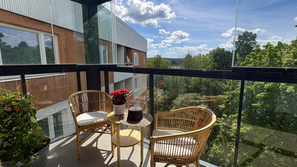 Innergård mellan flerbostadshus med ett gemensamt växthus, planteringar och ett stort lövträd. En grön och lugn utemiljö med sittplatser för de boende.