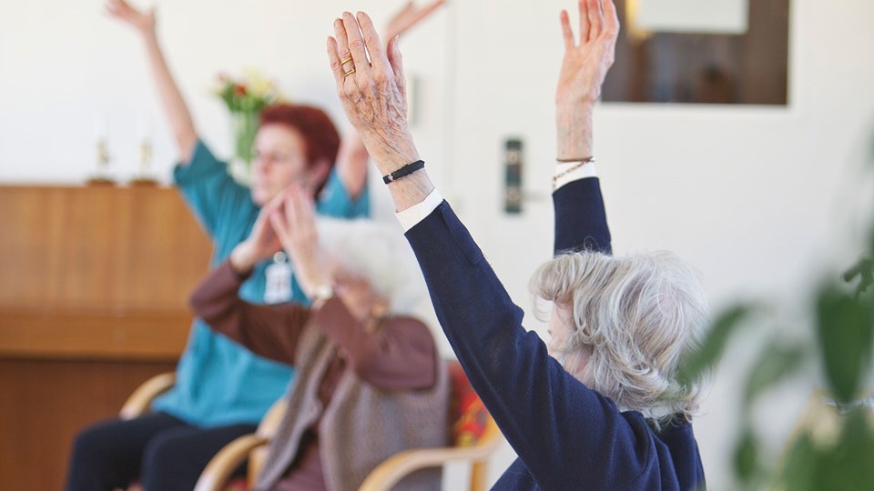 Äldre kvinnor som gör sitt-gymnastik tillsammans och sträcker upp armarna.