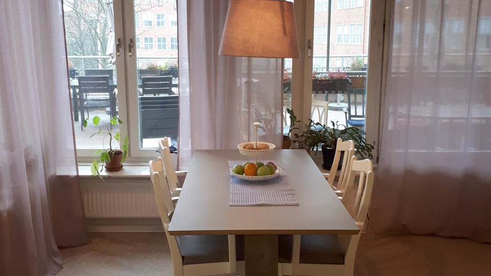 Bord med fyra stolar, taklampa och fruktskål på bordet framför fönster.