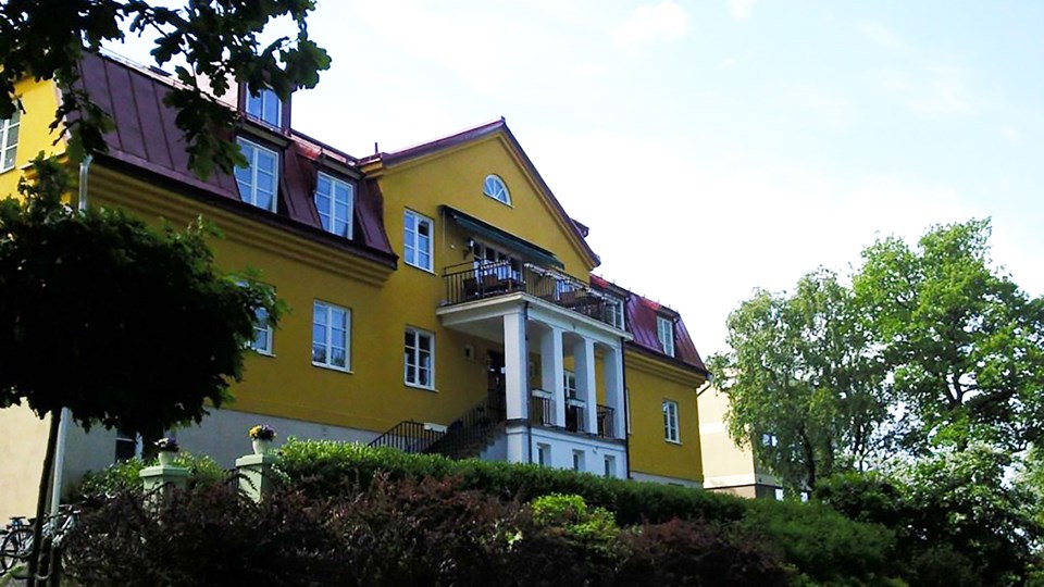 Stort hus med gul fasad och trädgård.