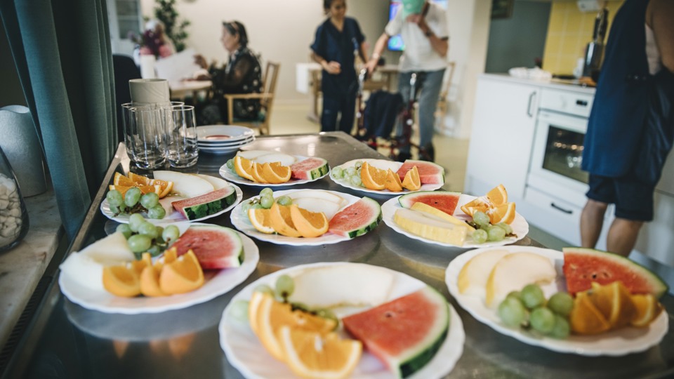 Uppdukade tallrikar med frukt i ett kök med människor