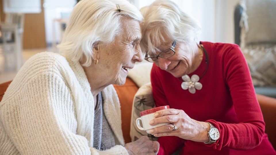 Två äldre kvinnor pratar och dricker kaffe.