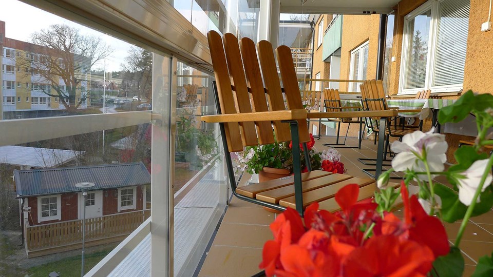 Fotografi på inglasad och möblerad balkong på boendet med utsikt på innegården.