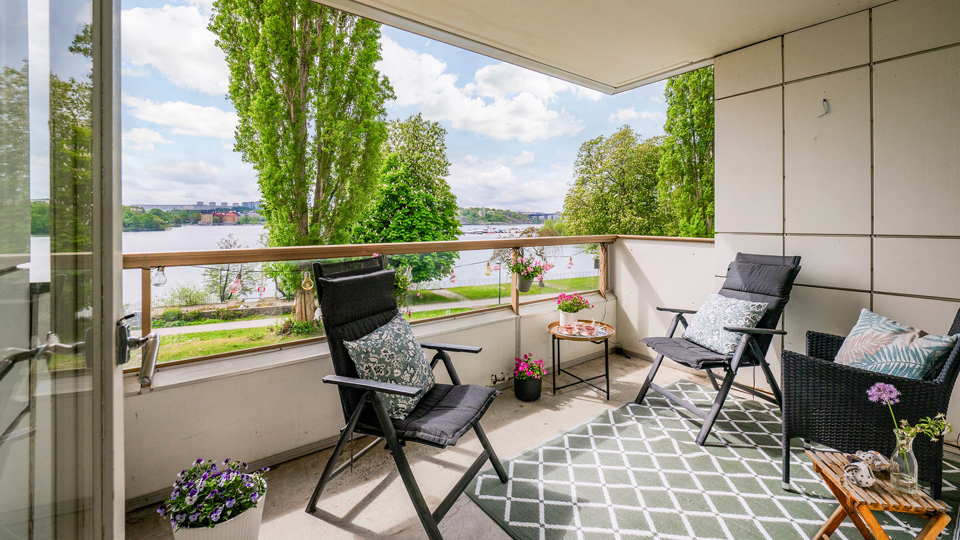 Utsikt mot vatten och träd från balkong, inredd med utemöbler.